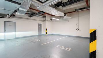 A parking garage with concrete floors, marked parking spaces, and visible ductwork on the ceiling.