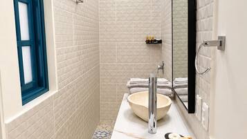 Une salle de bain avec un mur recouvert de carreaux blancs, un grand miroir, un lavabo et un espace douche.