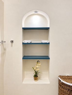 Un baño con una pared blanca, un estante azul con dos toallas blancas y una pequeña orquídea en maceta.