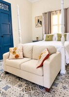 Un dormitorio con cama con dosel, un sofá con cojines decorativos, una mesita de noche con un florero y baldosas de suelo estampadas.