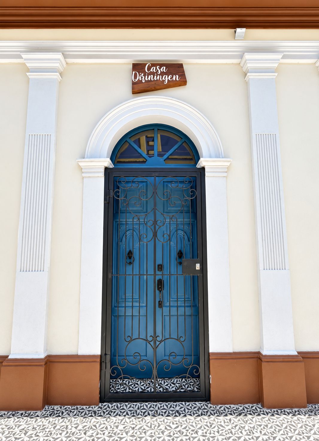 A blue door with a wrought iron gate, a sign above it, and a patterned tile floor.