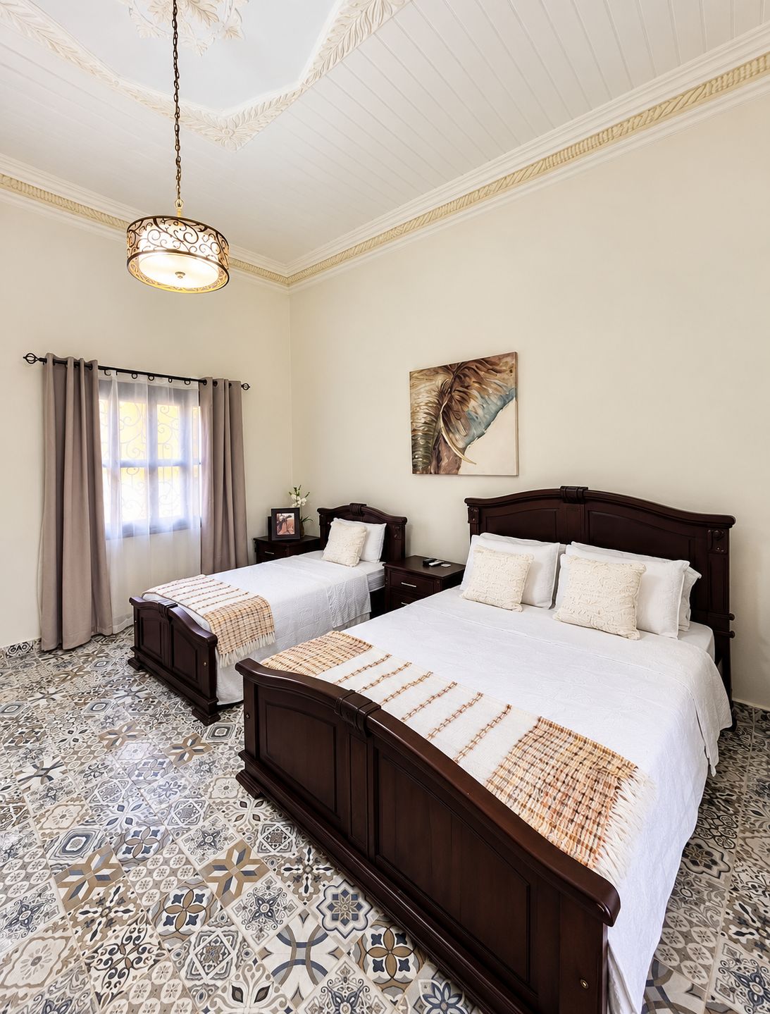 Habitación de hotel con dos camas, una araña, un cuadro y baldosas con diseño.