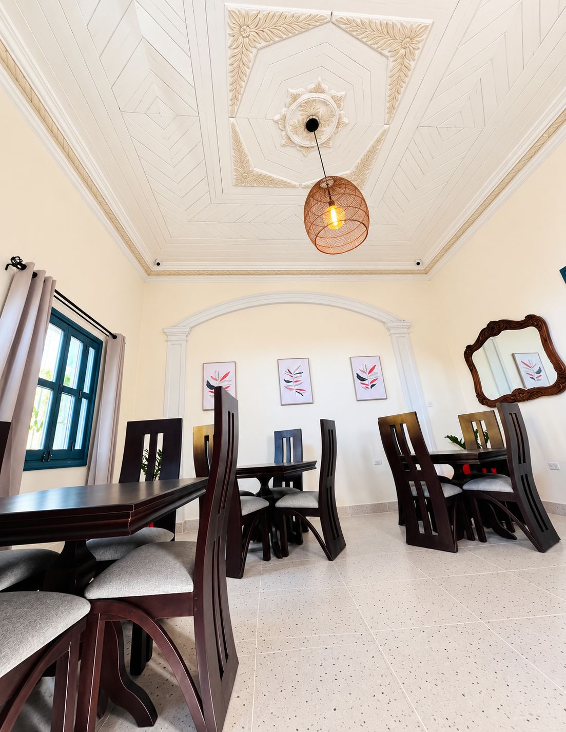 A dining area with a high ceiling, a chandelier, and a large mirror on the wall.