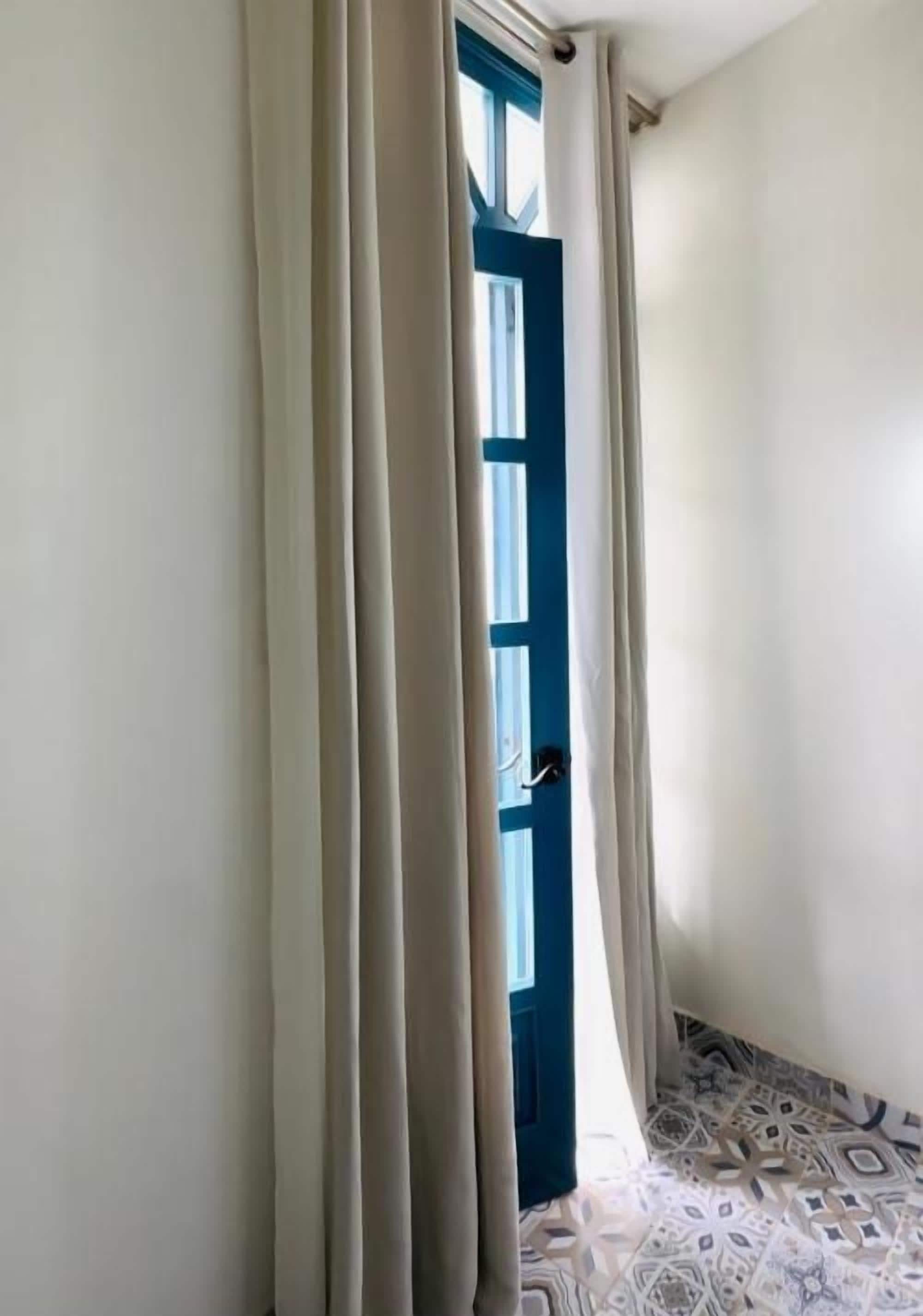 Un pasillo estrecho con una puerta azul y cortinas blancas.