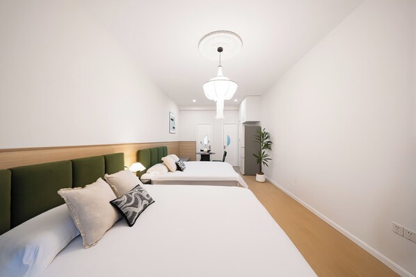 A hotel room with two beds, a wooden headboard, a bedside table with a lamp, and a potted plant.