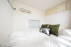 A bedroom with a bed, a window with blinds, a wall-mounted shelf with decorative items, and a wardrobe with a light-colored finish. - Tonight Homestay Jing'an Temple Shanghai Baicha Building (Shanghai)