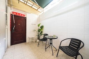 A small room with a wooden door, a white tiled wall, a potted plant, a table with a chair, and a small table with a mug. - Tonight Homestay Jing'an Temple Shanghai Baicha Building (Shanghai)