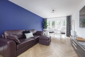 Ein modernes Wohnzimmer mit braunem Ledersofa, einem Esstisch mit Stühlen und einer Küchenzeile.