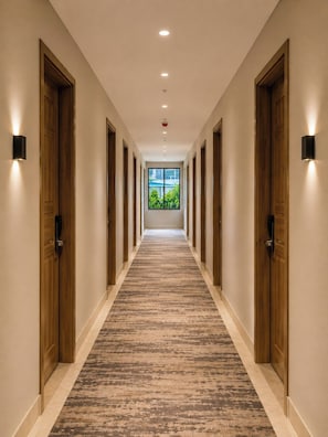 Un pasillo de hotel con puertas de madera, piso alfombrado e iluminación empotrada.