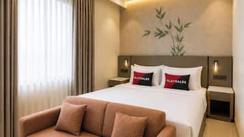 Ein modernes Hotelzimmer mit einem großen Bett, einem Standventilator, einer Wandlampe und einem Sofa.