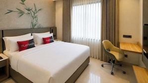 Ein Hotelzimmer mit einem Bett, einem Schreibtisch, einem Stuhl, einem Deckenventilator und einem Fenster mit Vorhängen.