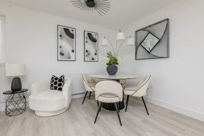 A modern dining area with a round table, two chairs, a vase with flowers, and abstract wall art. - South Queensferry 1 Bed with Iconic Bridge Views (Queensferry)