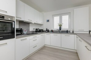 A modern kitchen with white cabinetry, a Bosch oven, and a window with blinds. - South Queensferry 1 Bed with Iconic Bridge Views (Queensferry)