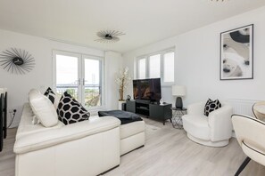 A modern living room with a sofa, armchair, and a television. - South Queensferry 1 Bed with Iconic Bridge Views (Queensferry)
