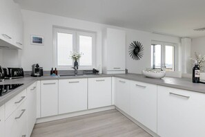 A modern kitchen with white cabinetry, a built-in oven, and a large window with blinds. - South Queensferry 1 Bed with Iconic Bridge Views (Queensferry)