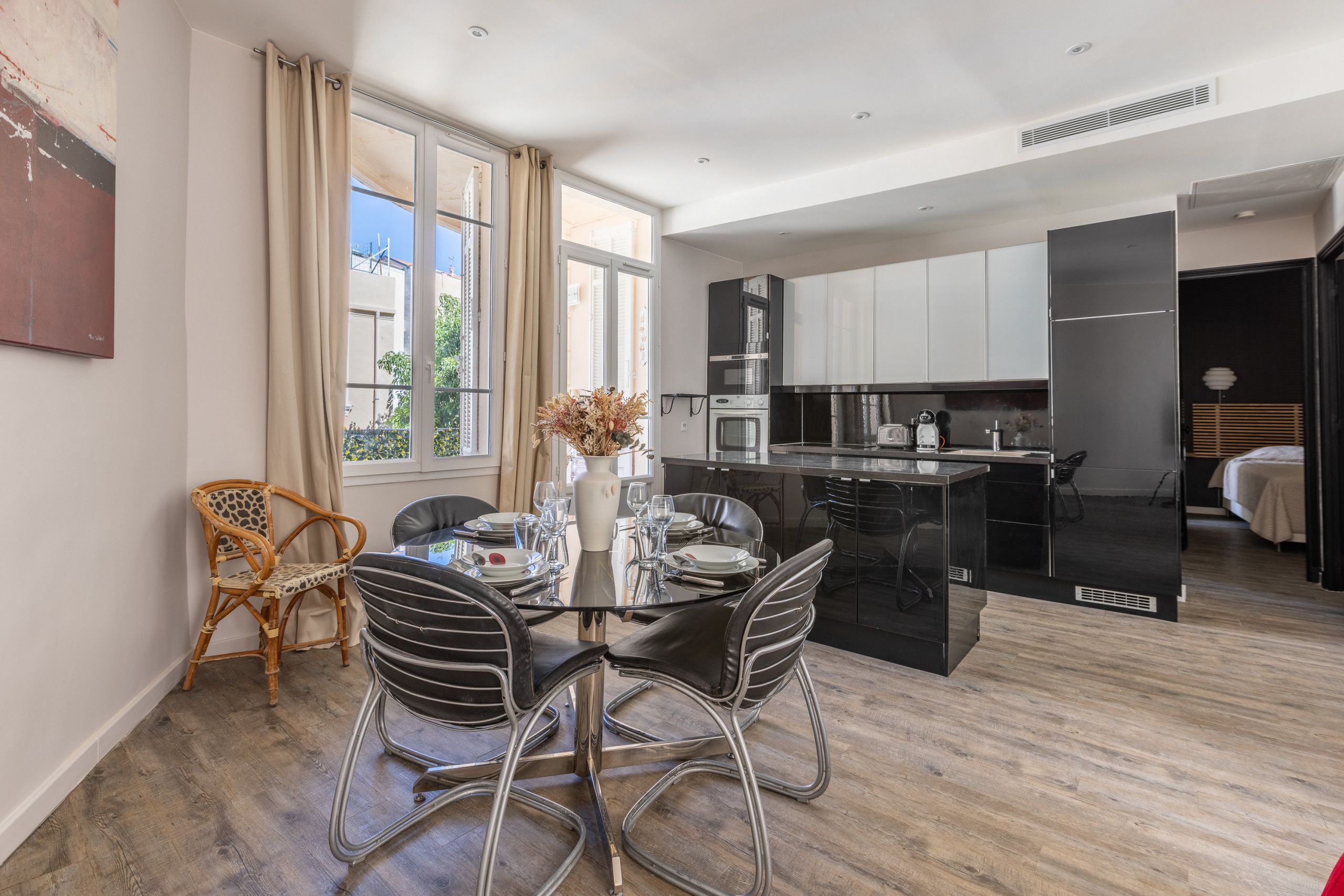 A modern kitchen with black appliances, a dining area with a glass table, and a view of the outside.