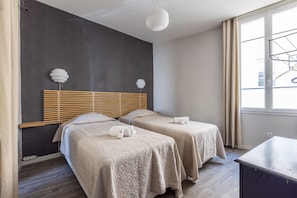 Ein Hotelzimmer mit zwei Betten, einem Holzkopfende, einem großen Fenster mit Vorhängen und einer Hängelampe.
