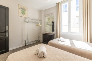 A hotel room with two beds, a wardrobe, a mirror, a drying rack, and a window with curtains. - Charming 2-Bedroom Apartment with Balcony in Forville A2B106 (Cannes)