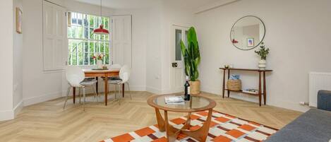 A modern living room with a dining area, a round coffee table, a large window with a view, and a mirror on the wall.