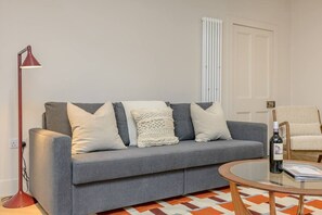 A modern living room with a grey sofa, a red floor lamp, a glass coffee table, and a patterned rug. - Central Stylish 1 Bed | Near Stockbridge (Edinburgh)