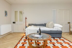 A modern bedroom with a bed, a bedside table with a bottle, a glass table, and a patterned rug. - Central Stylish 1 Bed | Near Stockbridge (Edinburgh)