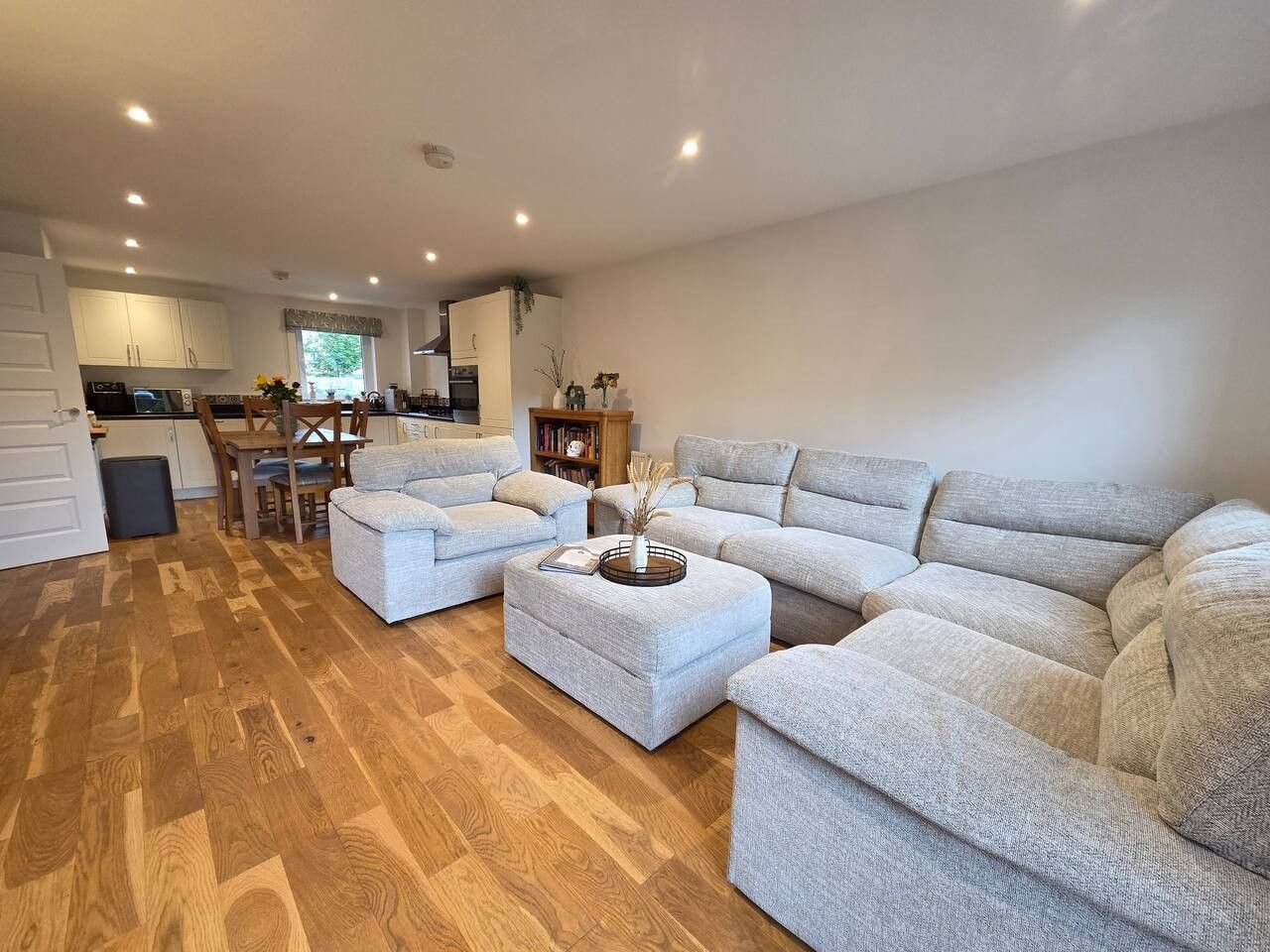 A spacious living area with a sofa set, ottoman, and a dining table with chairs.