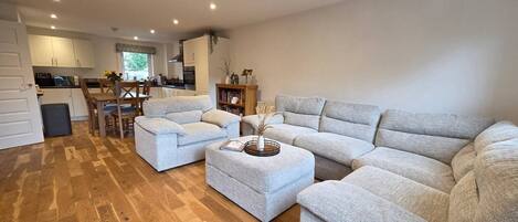 A spacious living area with a sofa set, ottoman, and a dining table with chairs.