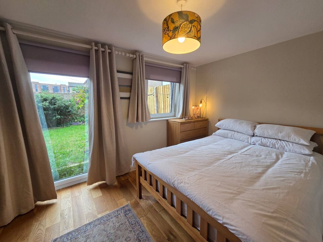 Ein Schlafzimmer mit Bett, Vorhängen, einem Fenster, einem Nachttisch und einer Lampe.