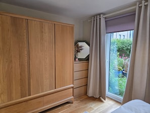 A bedroom with a wooden wardrobe, a bedside table with a mirror, and a window with curtains. - Portobello Garden Flat | 2 bed Near Beach (Edinburgh)