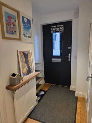Un couloir avec une porte noire, une fenêtre donnant sur un paysage et un radiateur.