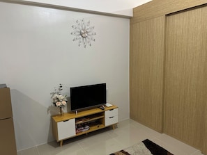A room with a flat-screen TV on a wooden TV stand, a decorative clock on the wall, and a wardrobe with sliding doors. - 1-Bedroom Condo with wifi, near SM North (Quezon City)