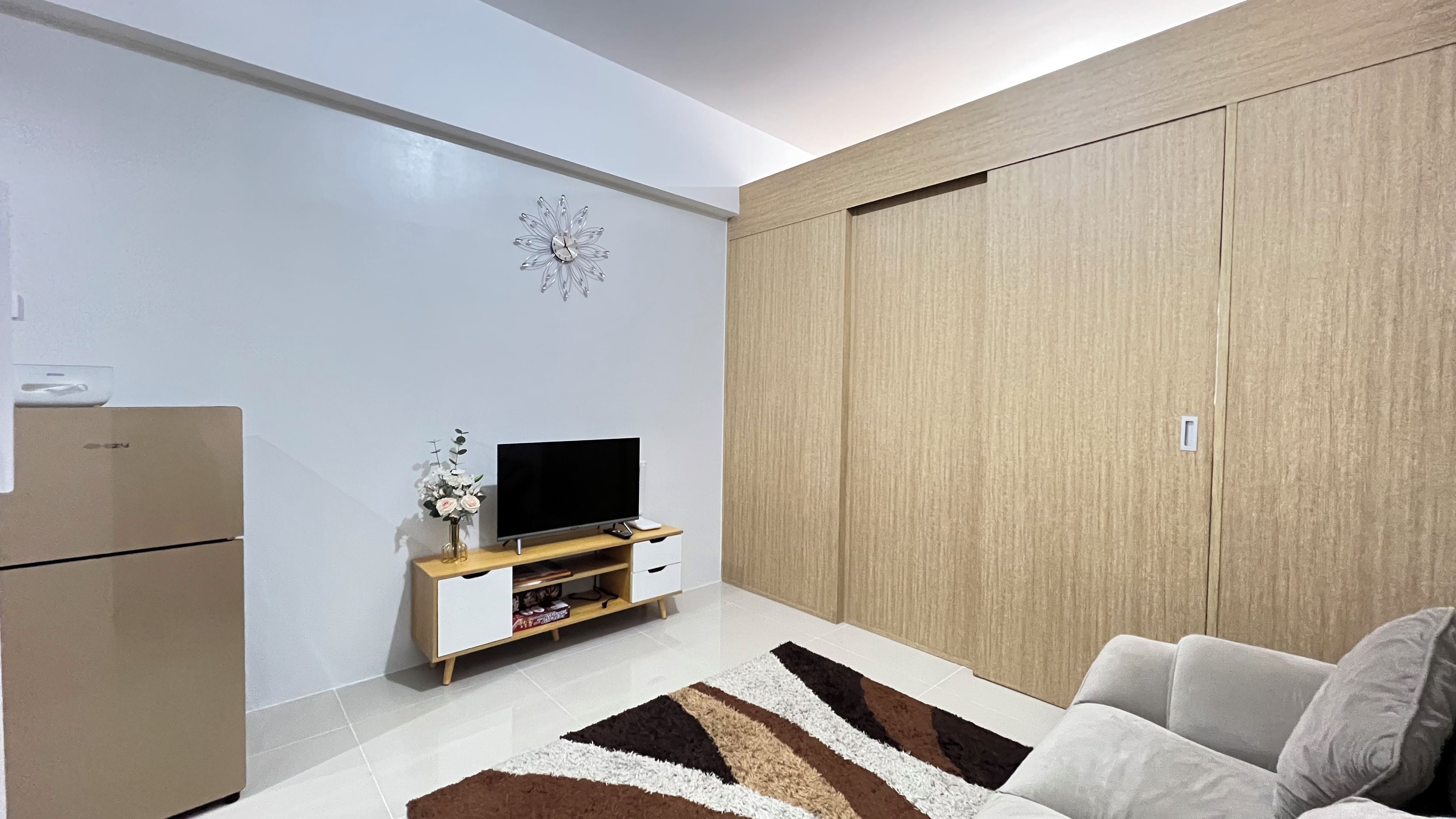 A modern living room with a flat-screen TV, wooden wardrobe, and a sofa.