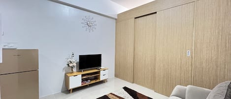 A modern living room with a flat-screen TV, wooden wardrobe, and a sofa.