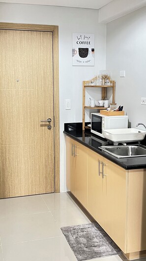 A modern kitchen with a wooden door, a microwave, a sink, and a coffee-themed wall art. - 1-Bedroom Condo with wifi, near SM North (Quezon City)