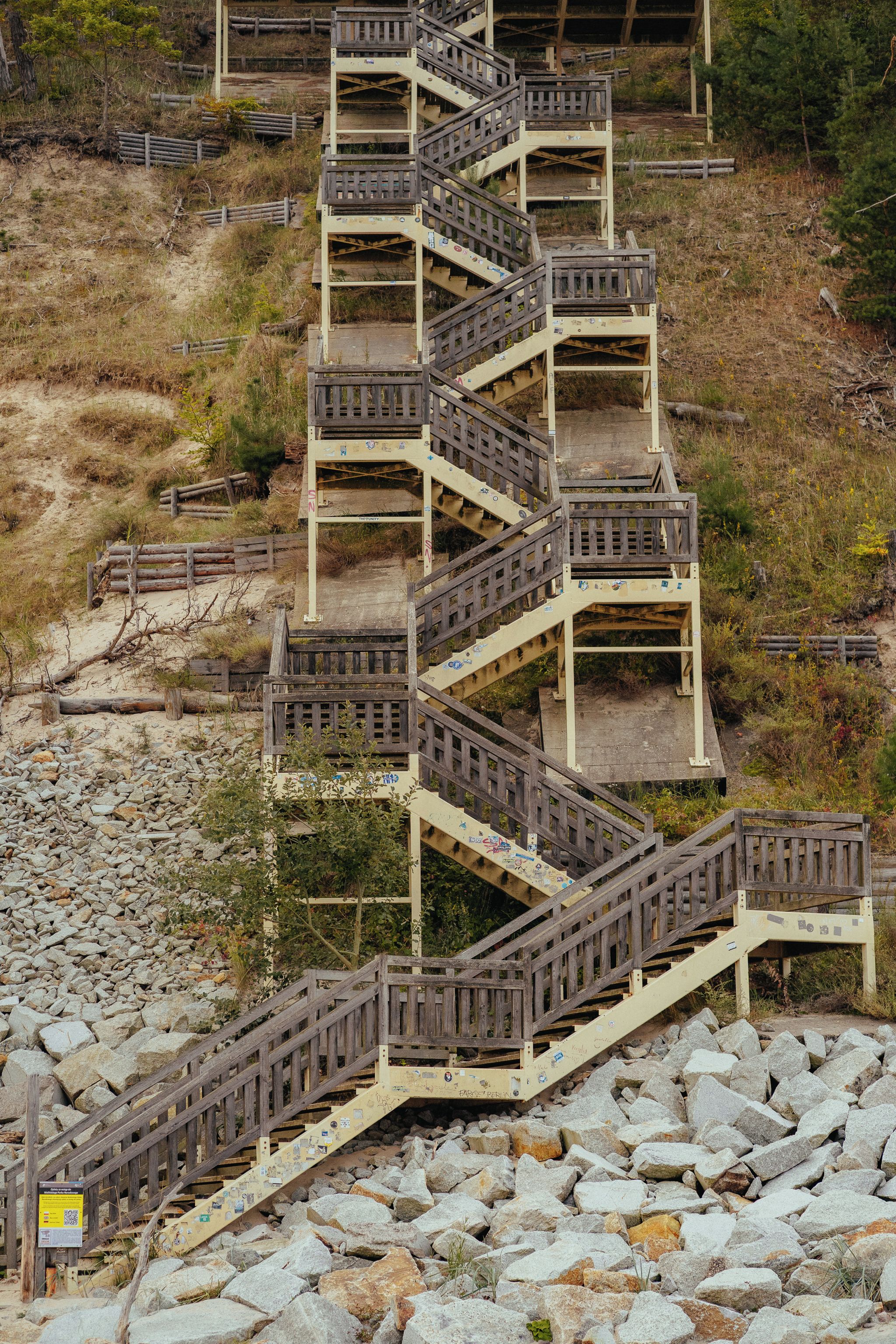 Eine mehrstufige Holztreppe, die über unwegsames Gelände mit spärlicher Vegetation führt.