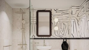Un baño moderno con cabina de ducha de vidrio, un lavamanos blanco con un florero negro y un espejo grande.