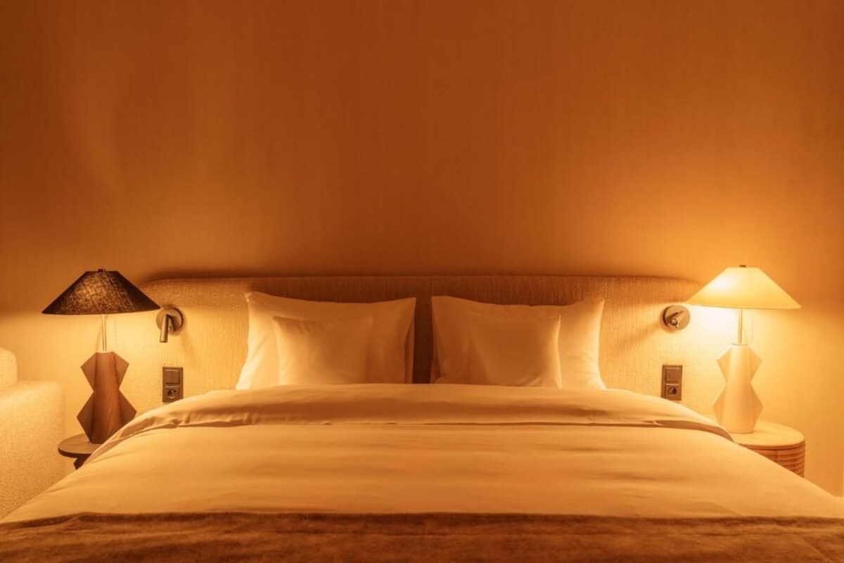 A hotel room with a bed, two bedside lamps, and a nightstand.