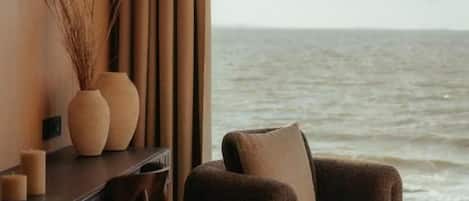 Une pièce avec vue sur la mer, une table ronde, un canapé et un bureau agrémenté d’un vase et de bougies.