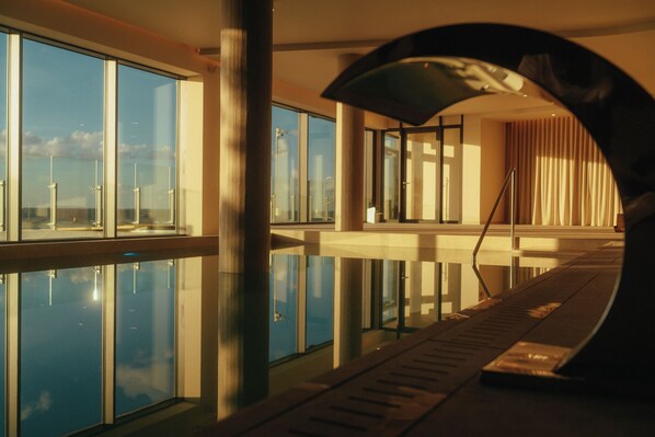 A modern hotel interior with a pool, large windows, and a view of the sky.