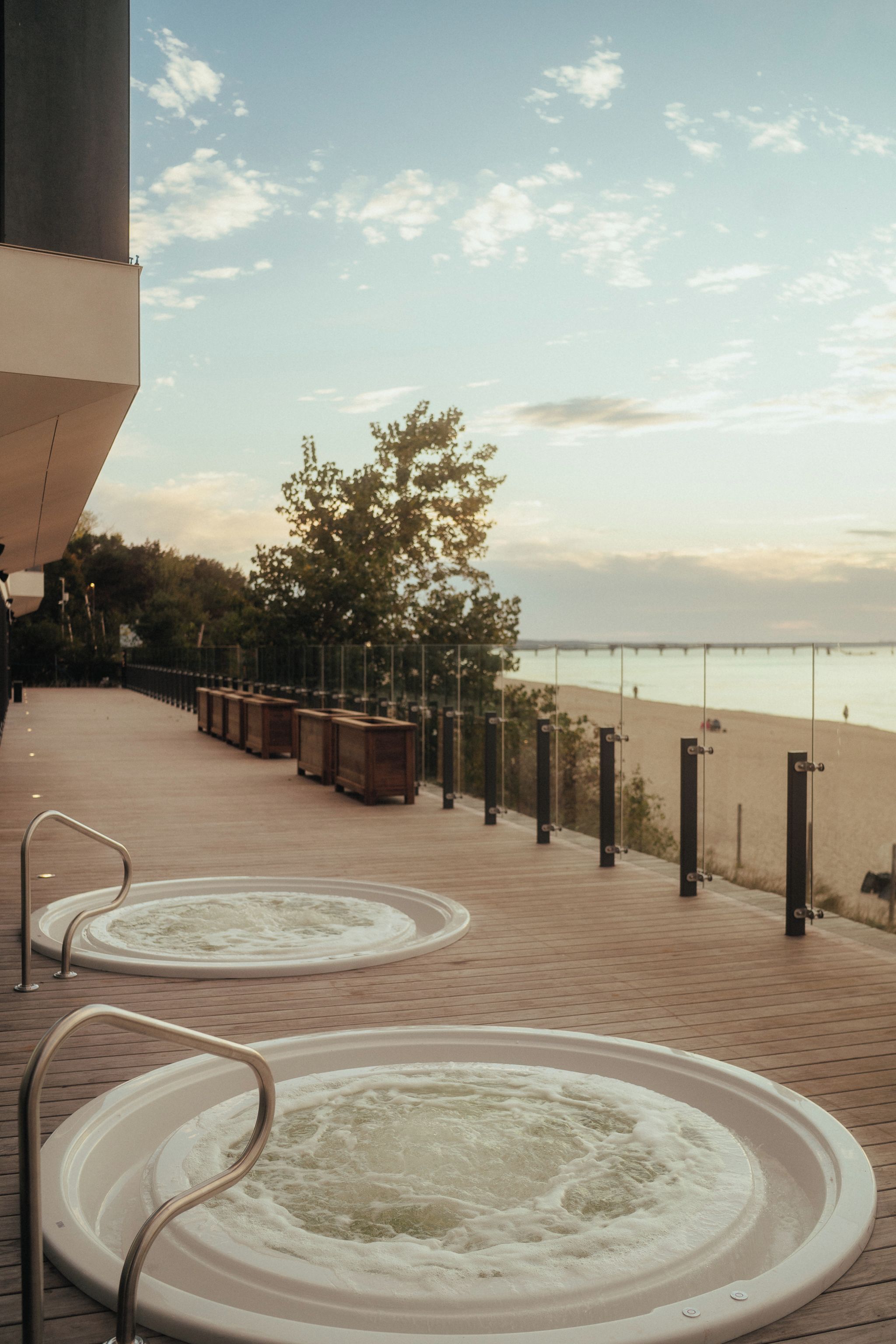 Un área de spa con dos jacuzzis, una terraza de madera y vistas a la playa.