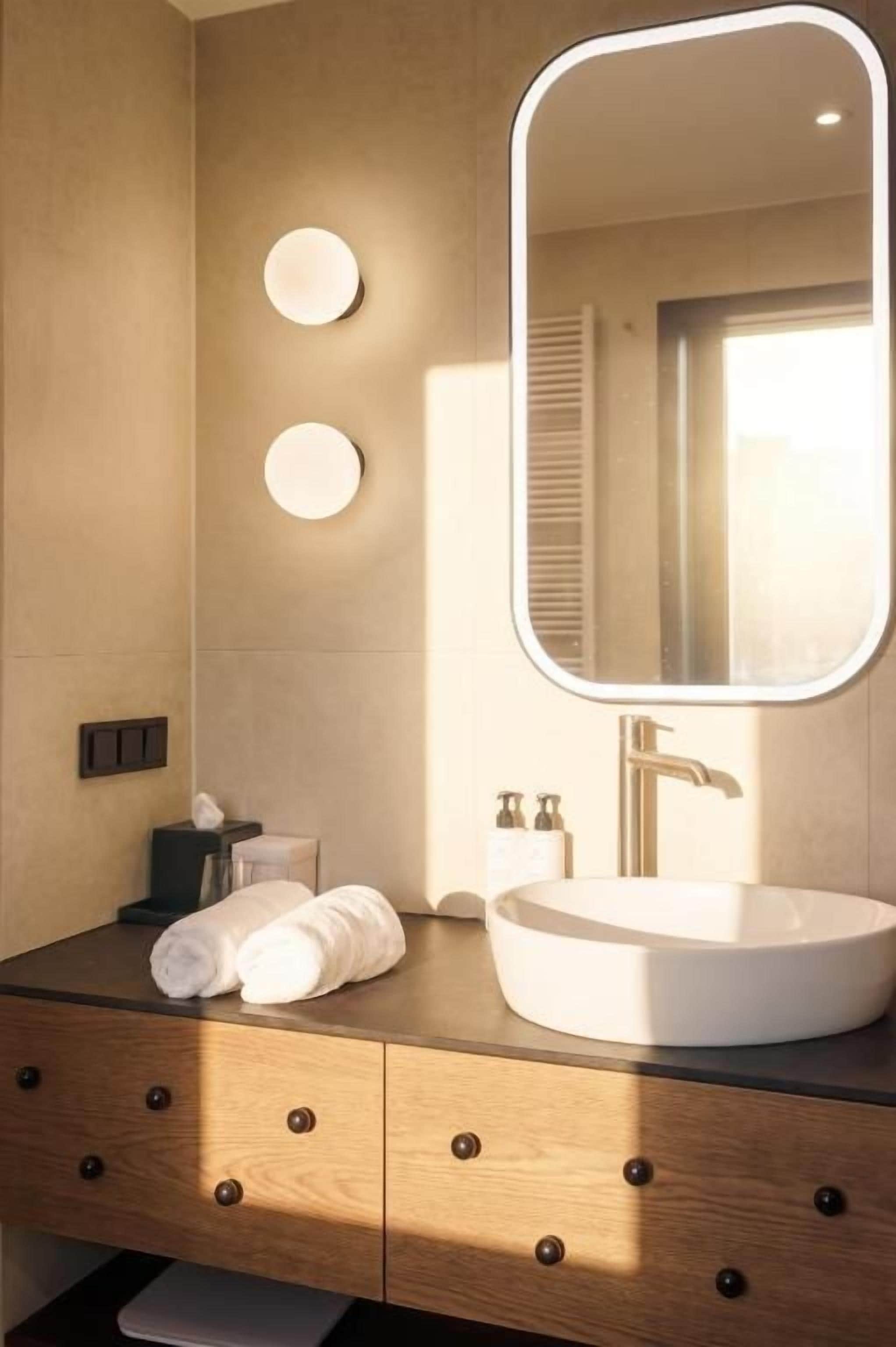 A bathroom with a round sink, a mirror with a light, and a towel on the counter.