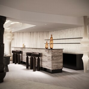 A modern bar area with a wooden counter, stools, and decorative vases.