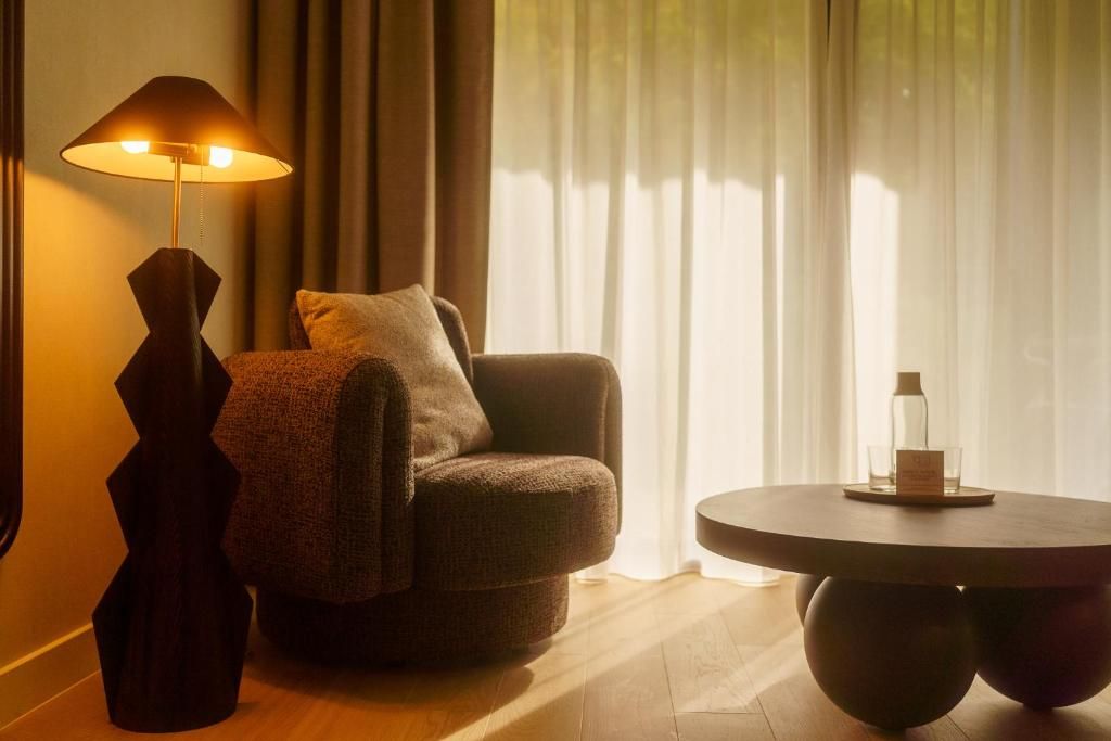 Une pièce chaleureuse avec une table ronde, une chaise, une lampe et une vue à travers de fins rideaux.