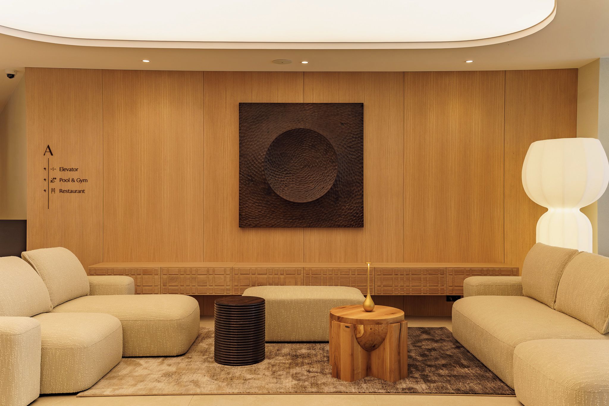 A modern living room with a sofa set, a round wooden side table, a tall floor lamp, and a wall-mounted artwork.
