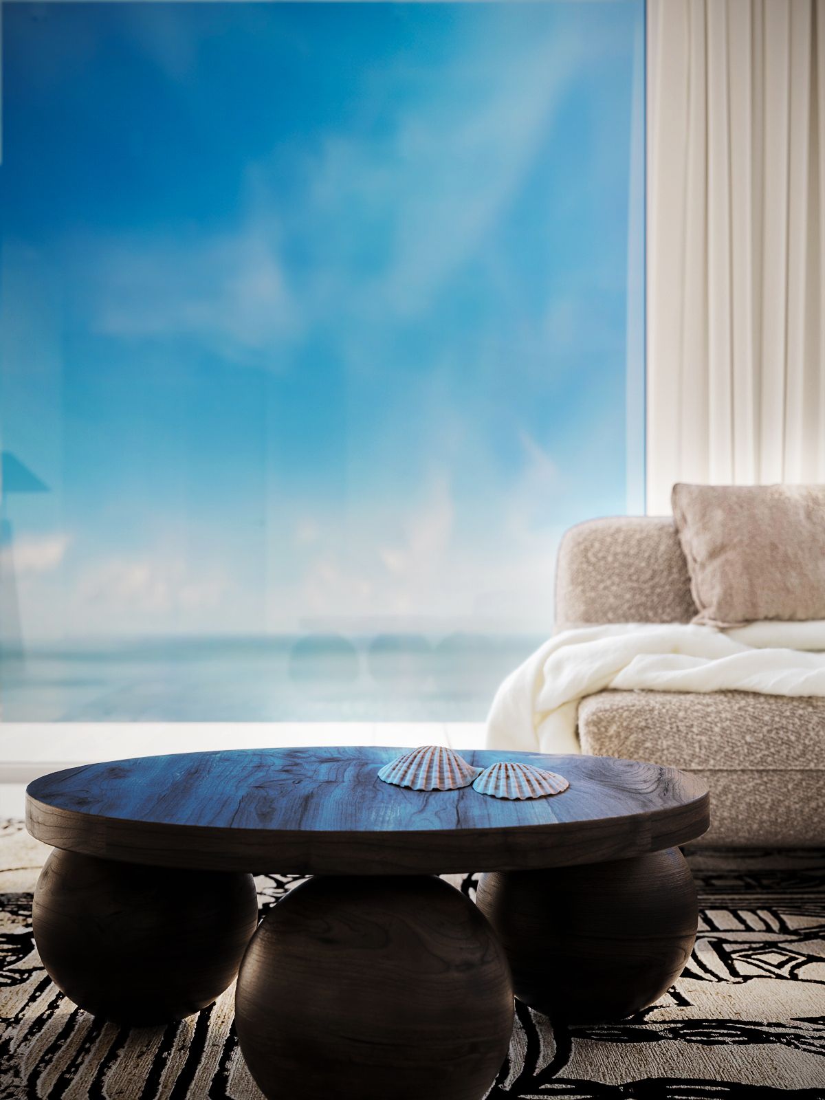 A round wooden table with a white cushion on top, placed in front of a window with a view of the sea.