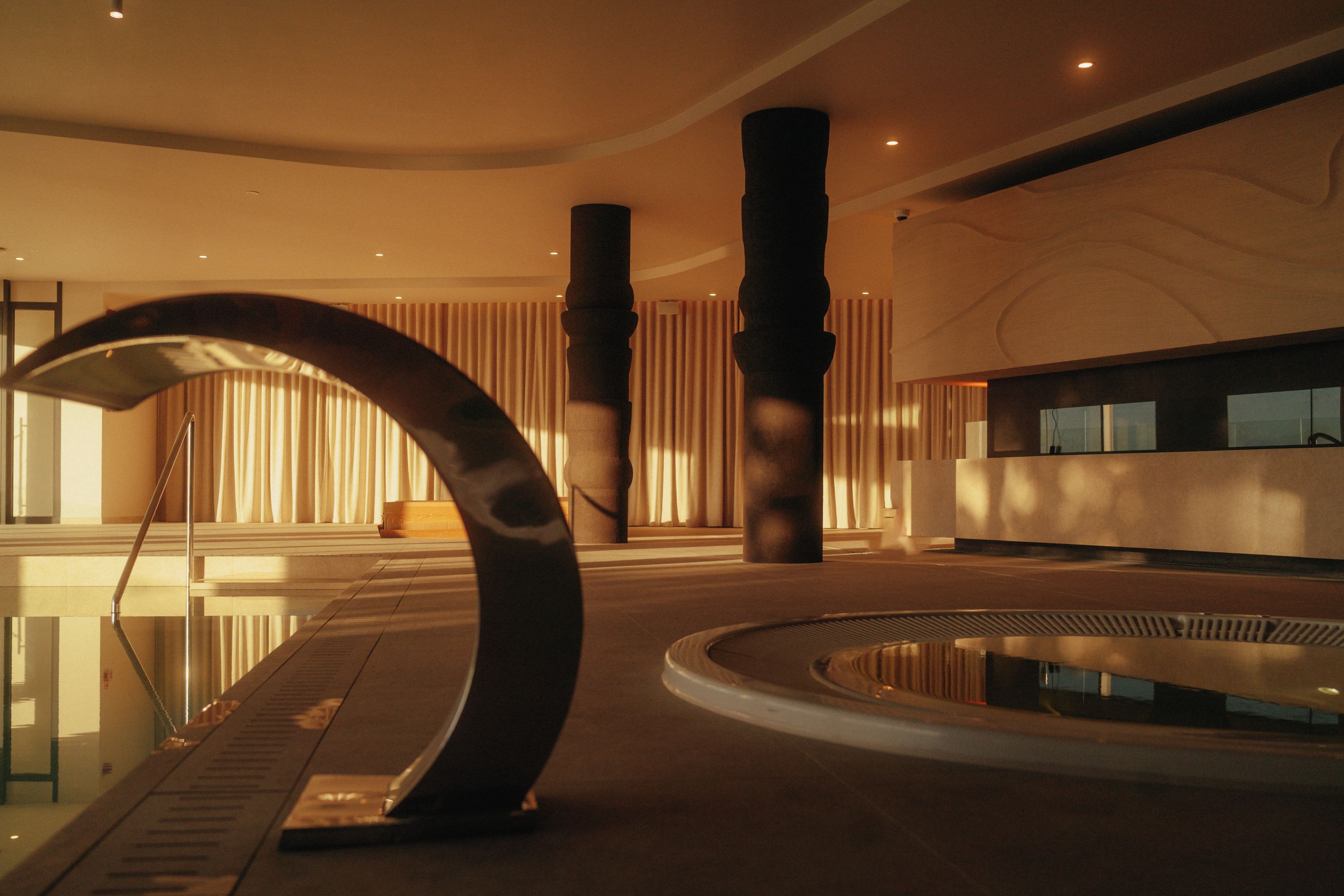 Ein modernes Interieur mit einer geschwungenen Metallskulptur, einem Pool und einem Empfangsbereich.