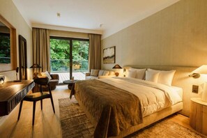Habitación de hotel con una cama grande, un escritorio, una silla, un sofá y vistas a zonas verdes.