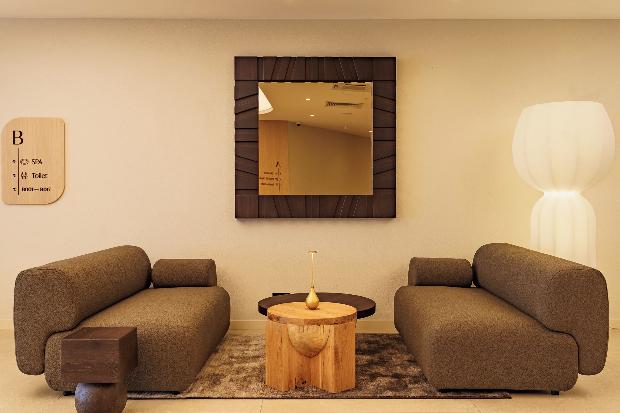 Ein modernes Wohnzimmer mit zwei Sofas, einem runden Holztisch und einem großen Spiegel an der Wand.