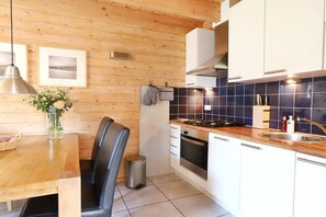 Eine moderne Küche mit Holzwänden, einem Essbereich mit Tisch und Stühlen sowie einer gefliesten Spritzschutzwand.