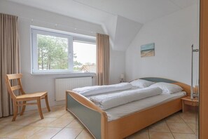 Ein Schlafzimmer mit einem Bett, einem Sessel, einem Fenster und einem Bild an der Wand.